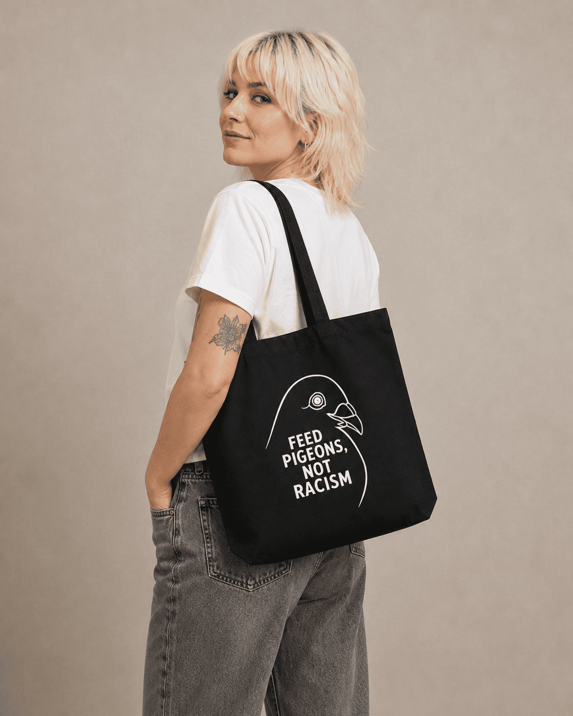 Ein blondes Model mit schlichter Kleidung trägt den Bio-Stoffbeutel mit Taubenkopf und dem Schriftzug "Feed Pigeons, Not Racism"
